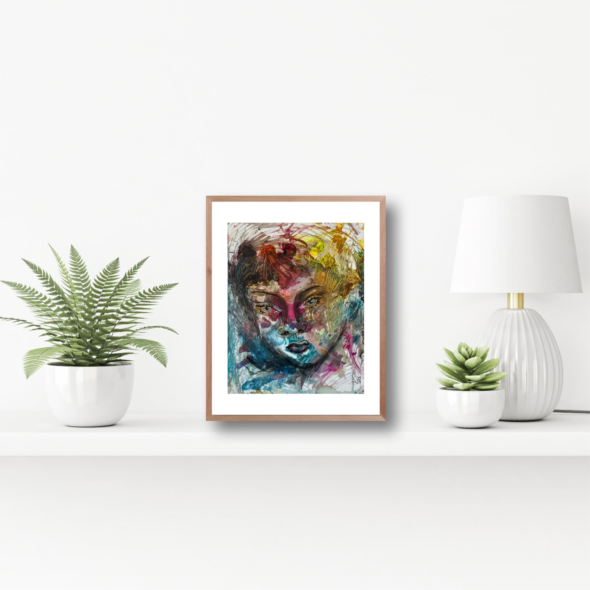 Framed abstract art painting on a white wall with decorative plants and a lamp.