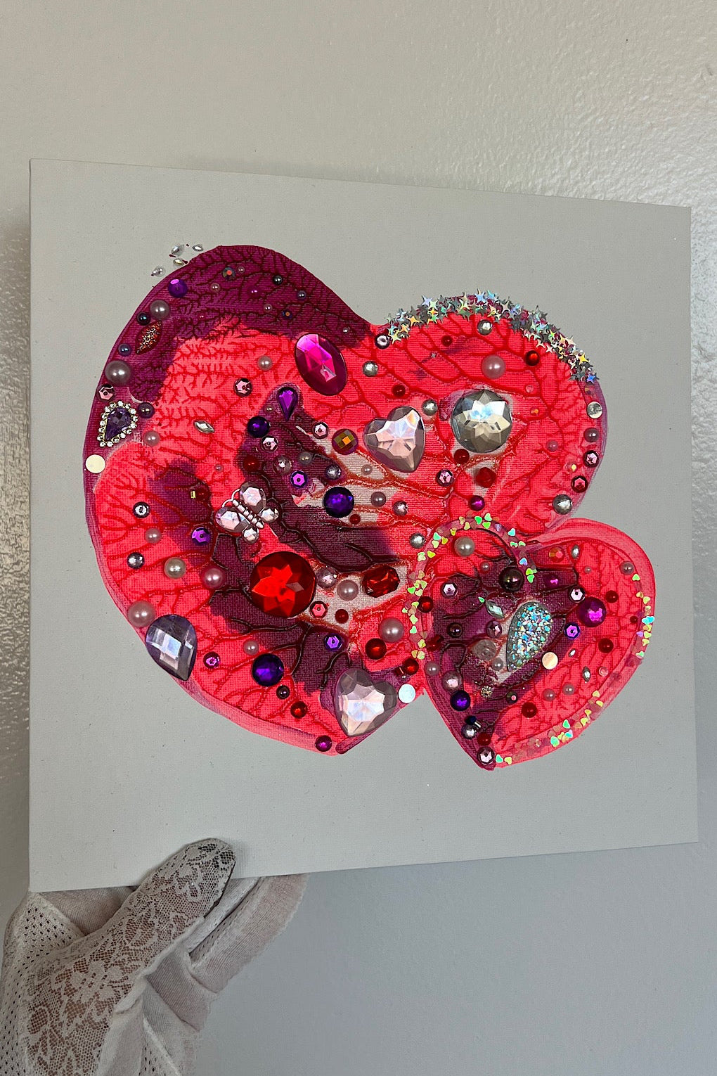 Decorative heart with sequins and beads on a white card, held by a hand.
