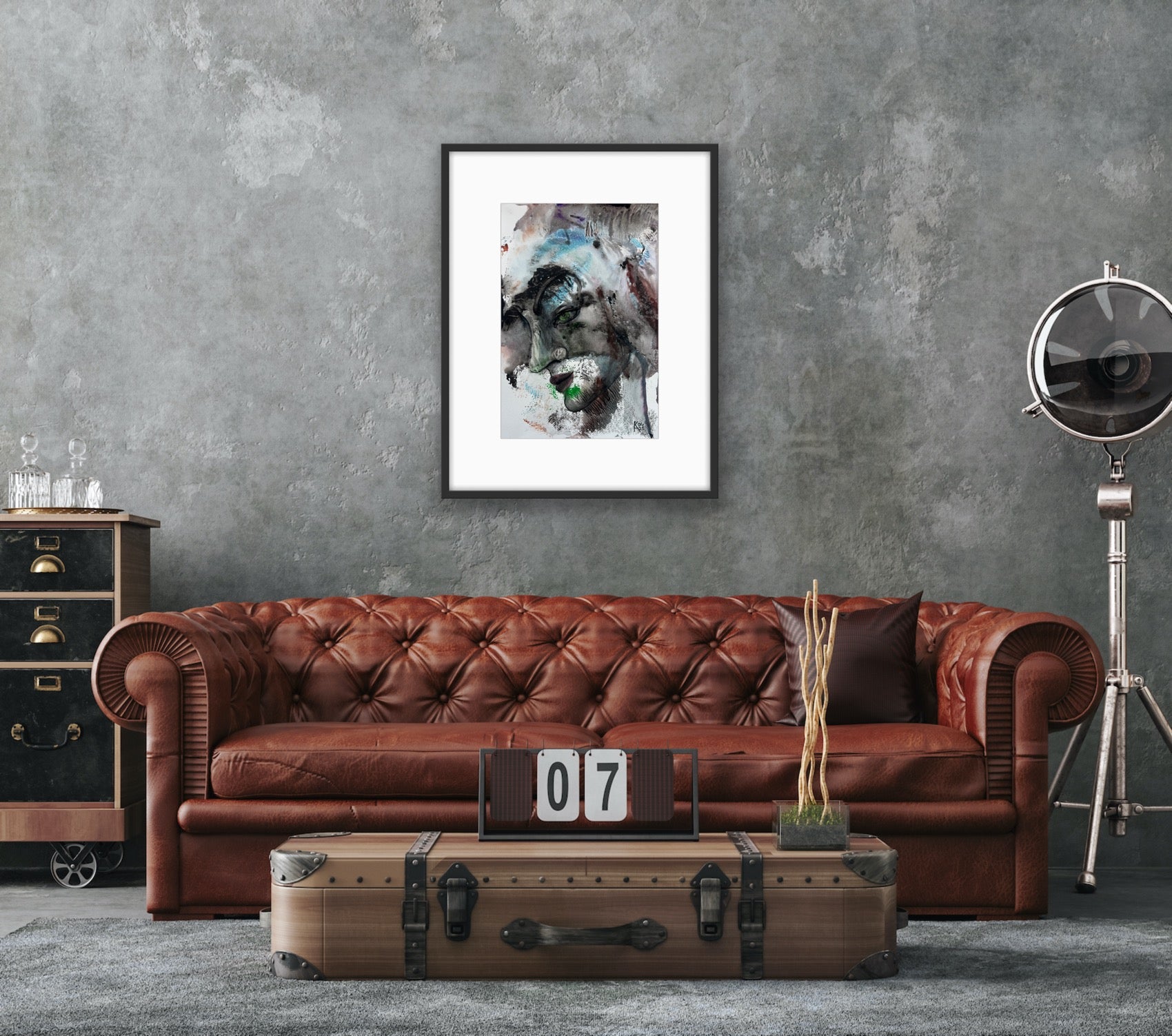 Brown leather sofa in a room with a textured gray wall, framed abstract art, and vintage suitcase.