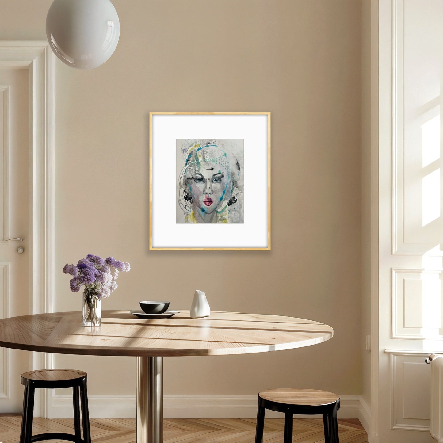 Watercolor art print in a gold frame displayed in a minimalist kitchen dining area with a light wood table, white pendant lamp, and purple flower arrangement
