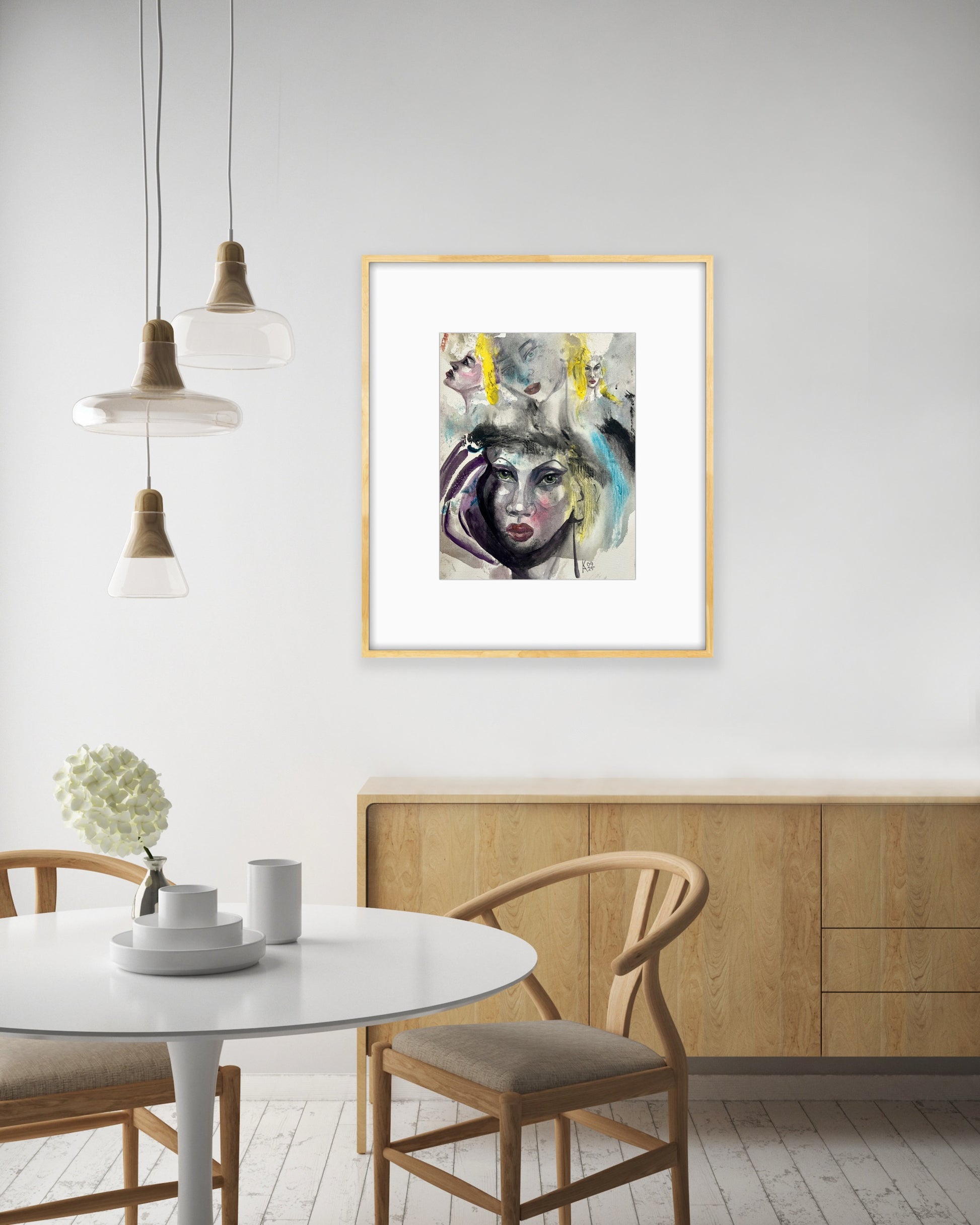 Gold-framed abstract woman watercolor painting hanging over a wooden sideboard in a bright dining room setting.
