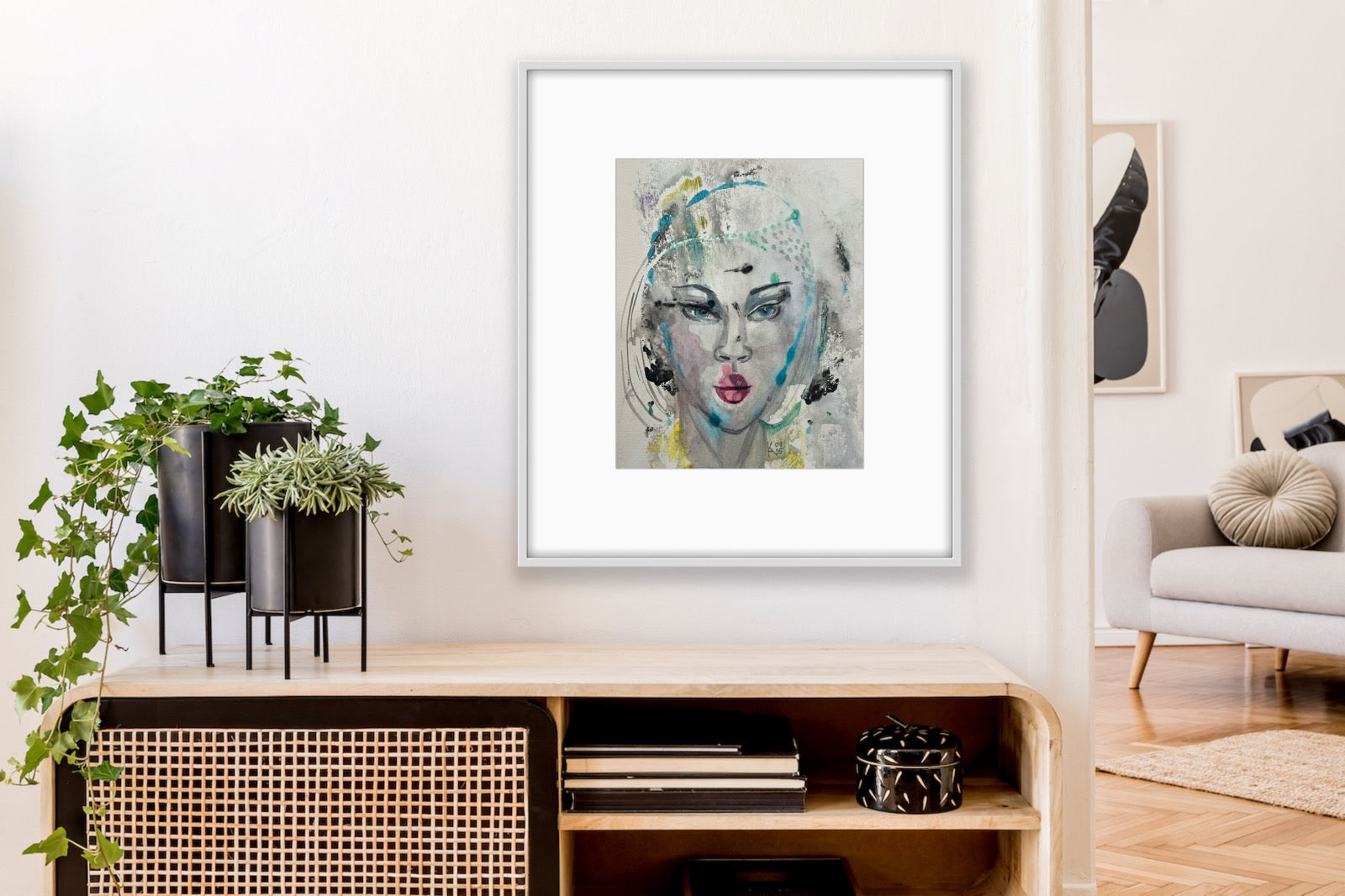 Framed mixed-media portrait artwork hanging in a modern living room above a wooden shelf with potted plants and books