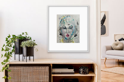 Framed mixed-media portrait artwork hanging in a modern living room above a wooden shelf with potted plants and books