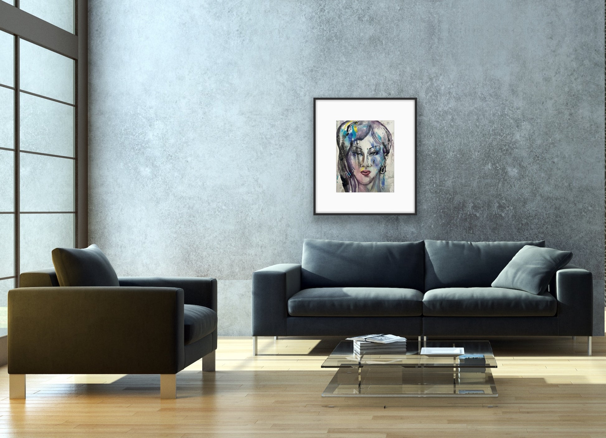 Framed watercolor abstract face art hanging on a textured grey concrete wall in a minimalist living room, positioned above a dark charcoal sofa and a glass coffee table with books and natural sunlight