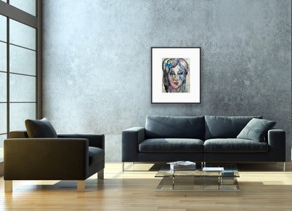 Framed watercolor abstract face art hanging on a textured grey concrete wall in a minimalist living room, positioned above a dark charcoal sofa and a glass coffee table with books and natural sunlight