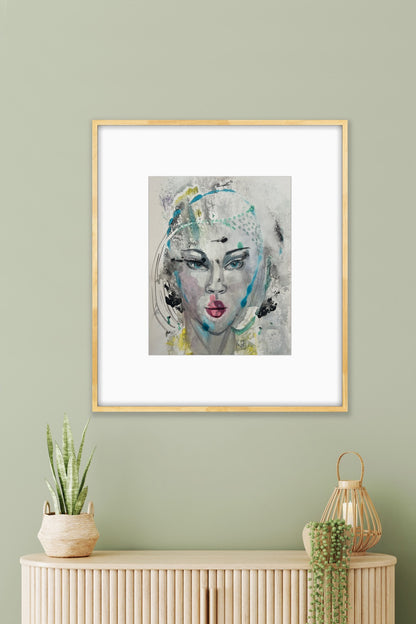 Framed mixed-media portrait artwork hanging on a sage green wall, styled with a snake plant and lantern decor on a light wood credenza
